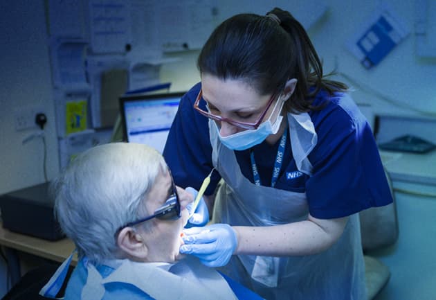 Community Dentistry Web Appetiser Ad 630X433px A female NHS dentist examining an elderly patient