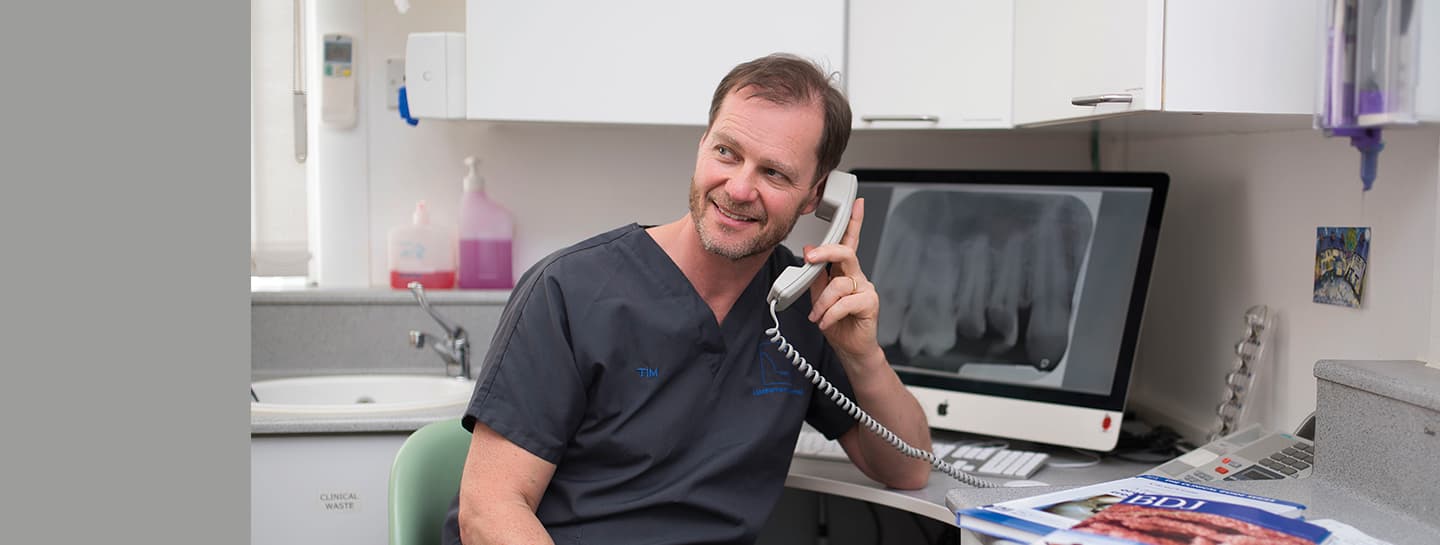 Advice hero launch A dentist wearing dark grey scrubs is on the phone at a desk in a dental surgery