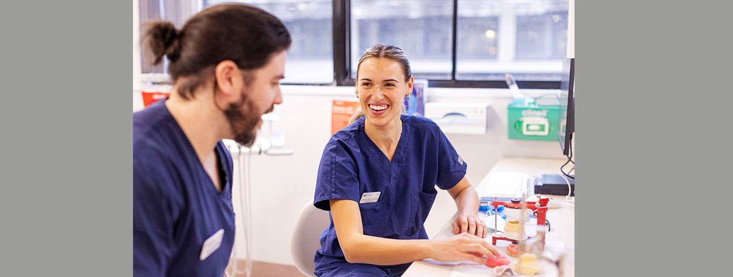 Graduate Membership Hero Image A graduate dentist by a desk smiling at a colleague